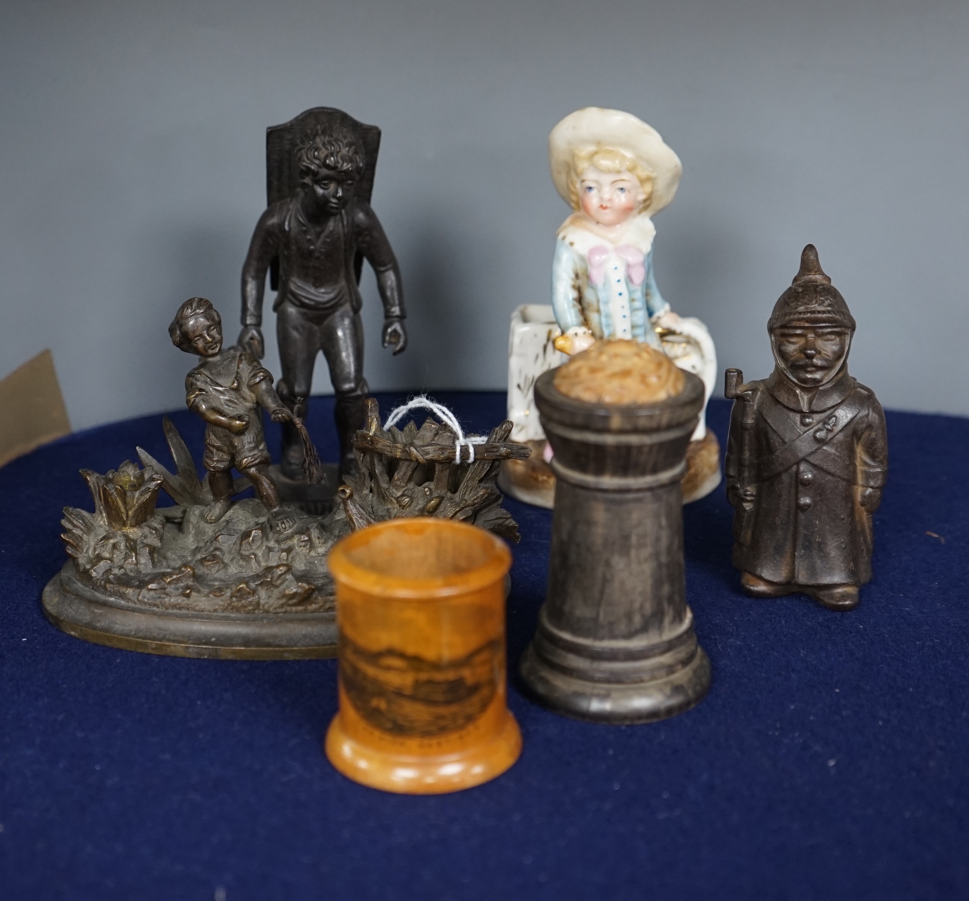 Six match tidies / strikers, including in the form of a WWI German soldier in trench coat and pickelhaube, a Mauchline ware pot with image of Hastings Pier, a cast metal figure of a boy, etc. Condition - fair